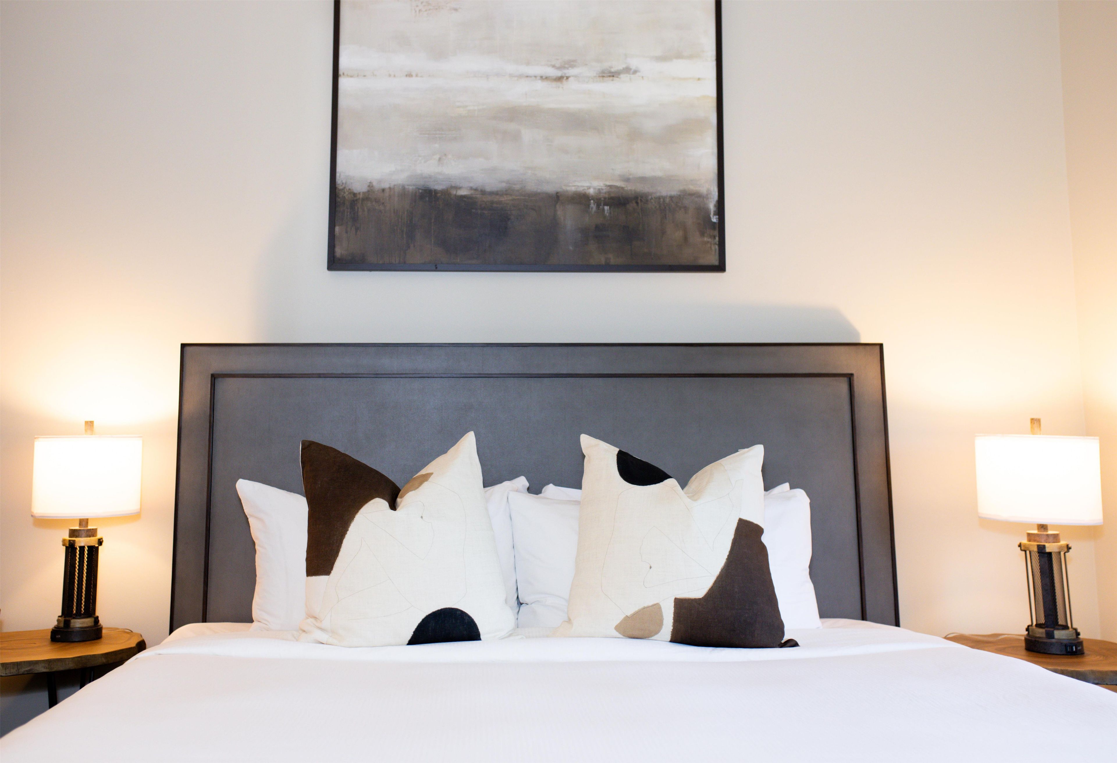 A hotel room with a large bed, two bedside lamps, and a painting above the bed.