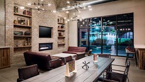 A modern living room with a brick wall, a fireplace, a large window, and a dining area. - Watt Hotel Rahway, Tapestry Collection by Hilton (Rahway)