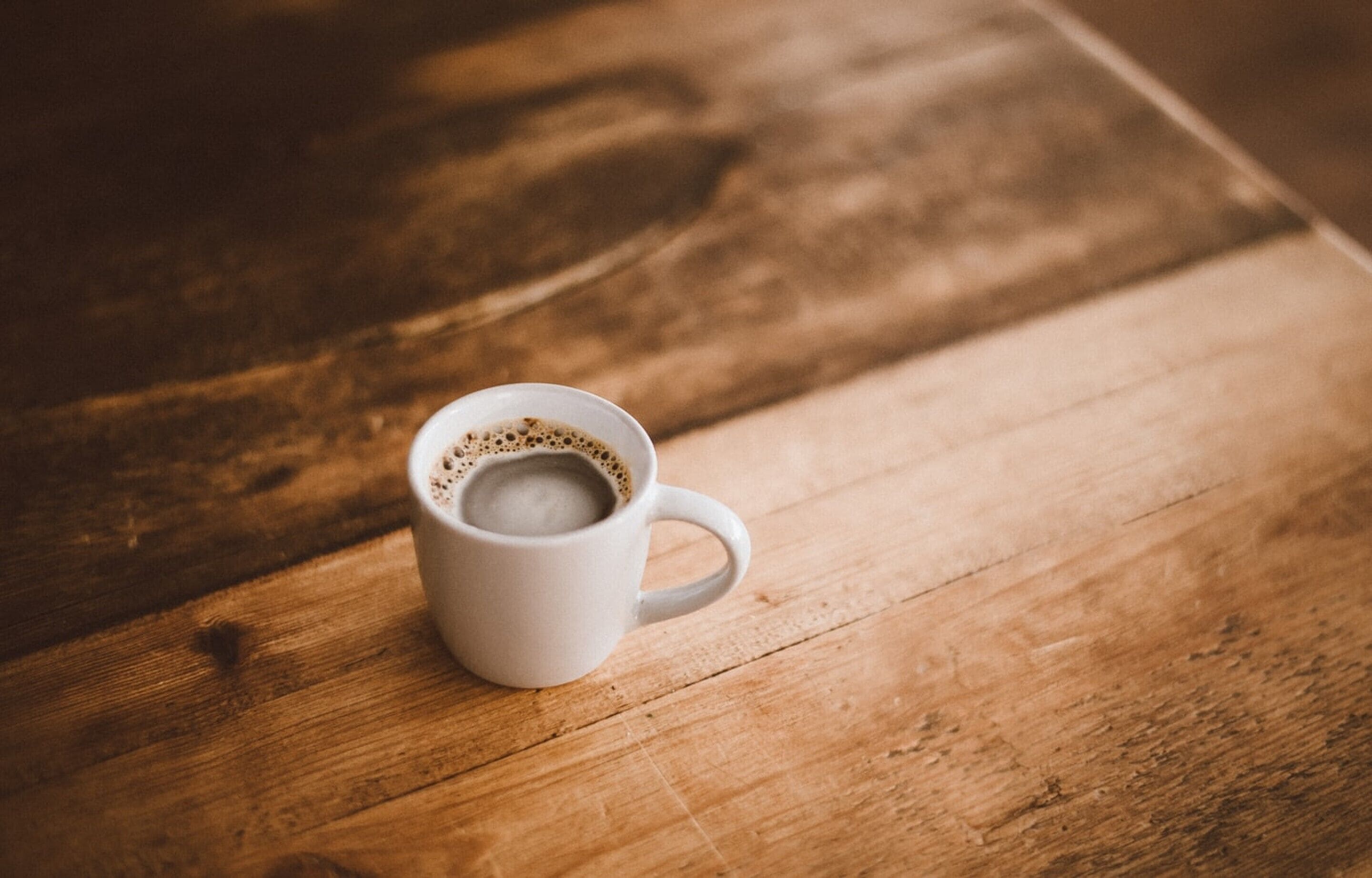 A white mug with coffee on a wooden table.