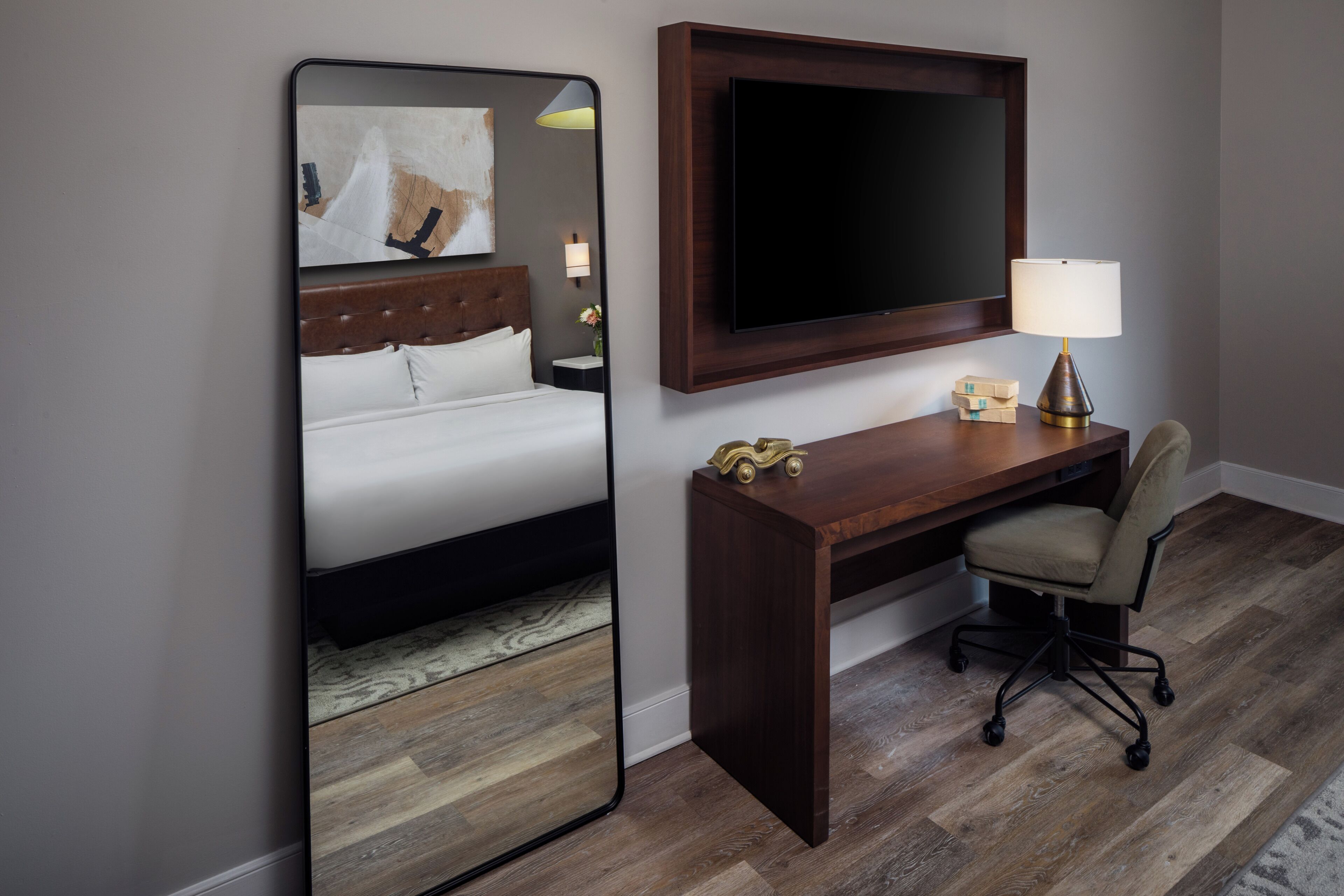 A hotel room with a bed, a desk, a chair, a TV, and a mirror.