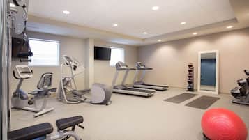 A gym with treadmills, elliptical machines, a bench, and exercise balls.