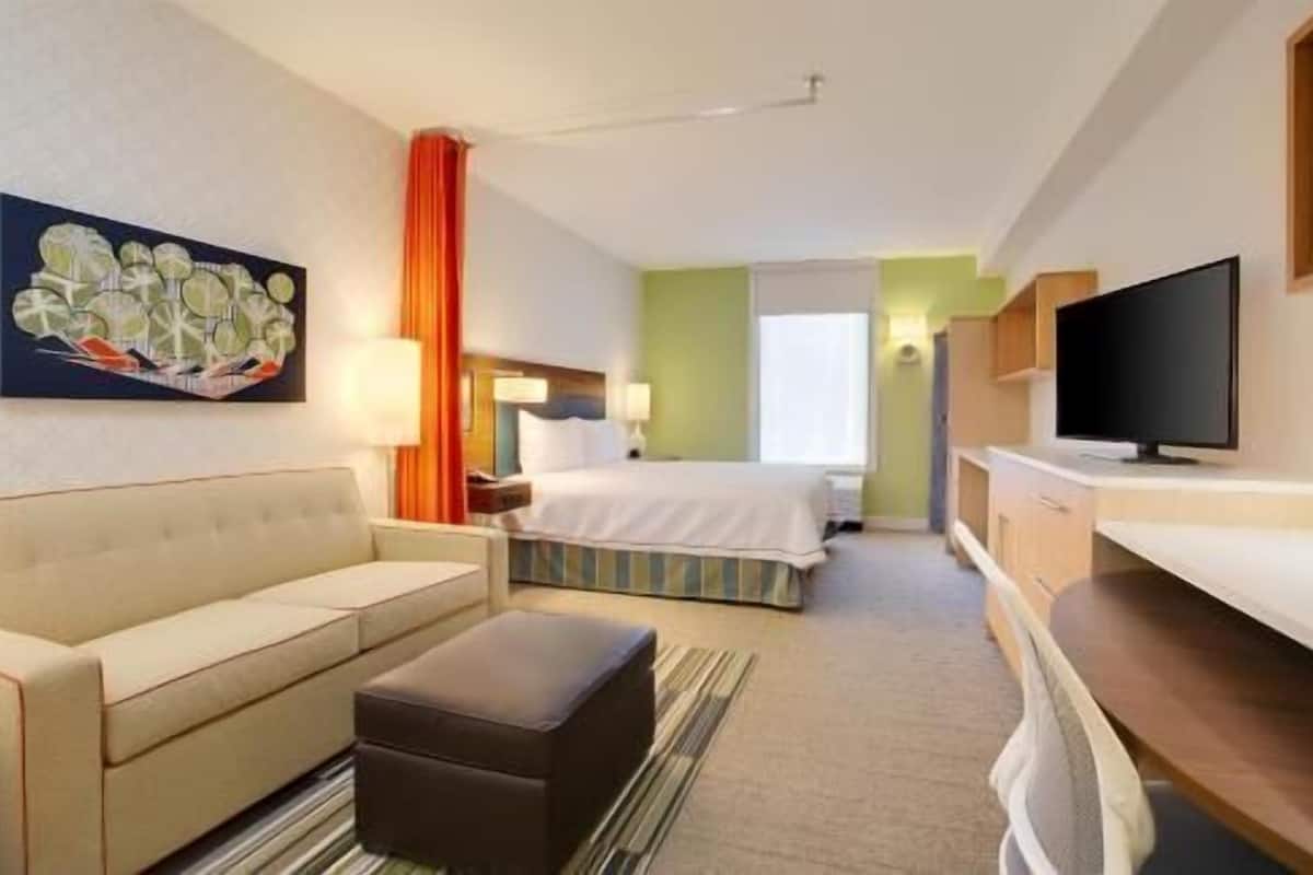 A hotel room with a bed, a sofa, a TV, and a painting on the wall.
