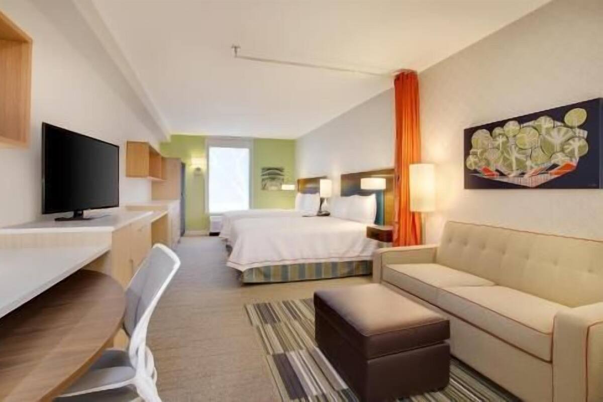 A hotel room with a TV, a desk, a bed, a sofa, and a painting on the wall.