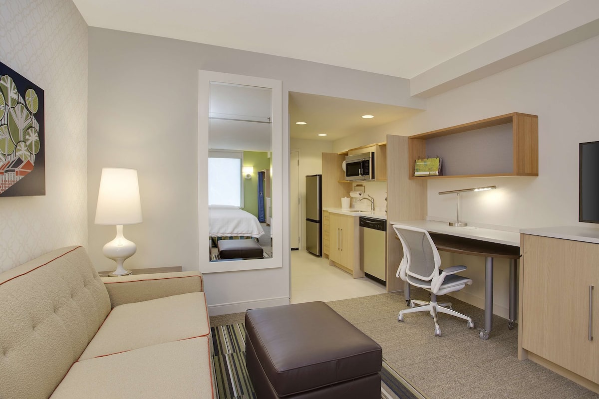 A hotel room with a bed, a desk, a chair, a television, and a kitchenette.