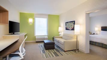 Habitación de hotel con escritorio, sofá, cama, televisor y ventana.