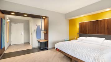 A modern hotel room with a large bed, a wooden headboard, a small side table, and a wardrobe.