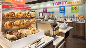 A breakfast area with a variety of bagels and donuts displayed in a glass case, a coffee station, and a sign advertising 'Top It Breakfast' with yogurt, oatmeal, and fruit options. - Tru by Hilton Cheyenne WY (Cheyenne)