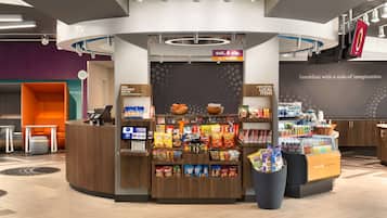 A 24/7 market kiosk with a variety of snacks and beverages, a coffee station, and a seating area with a modern design.