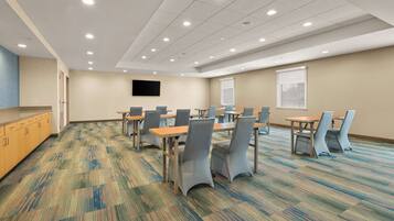 A conference room with a carpeted floor, tables, chairs, a flat-screen TV, and a window.