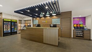 A hotel reception area with a wooden reception desk, a minibar, and a coffee and tea station. - Home2 Suites by Hilton Baytown (Baytown)