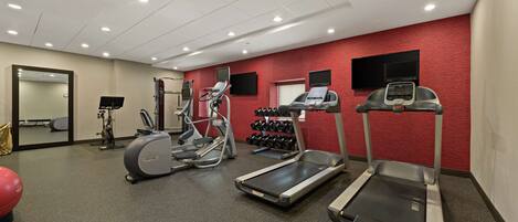 A gym with treadmills, elliptical machines, and a wall-mounted TV.