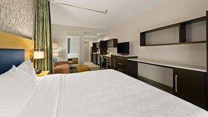 A hotel room with a large bed, a desk, a television, and a kitchenette. - Home2 Suites by Hilton Baytown (Baytown)
