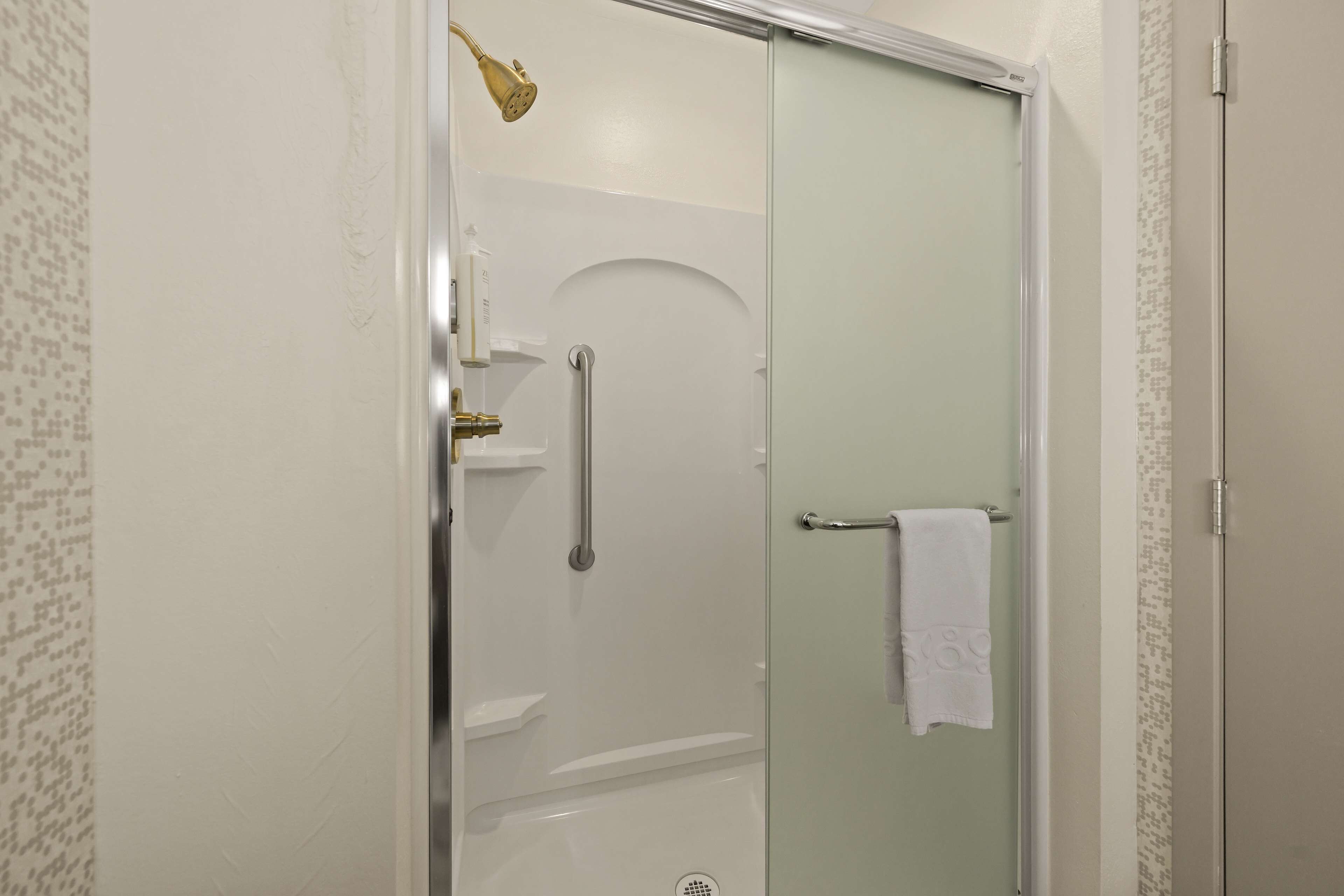 A glass-enclosed shower with a handheld showerhead, a towel rack, and a door with a towel hanging on it.