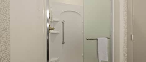 A glass-enclosed shower with a handheld showerhead, a towel rack, and a door with a towel hanging on it.