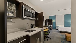 A compact hotel room with a kitchenette, a bed, a desk, and a bathroom. - Home2 Suites by Hilton Baytown (Baytown)