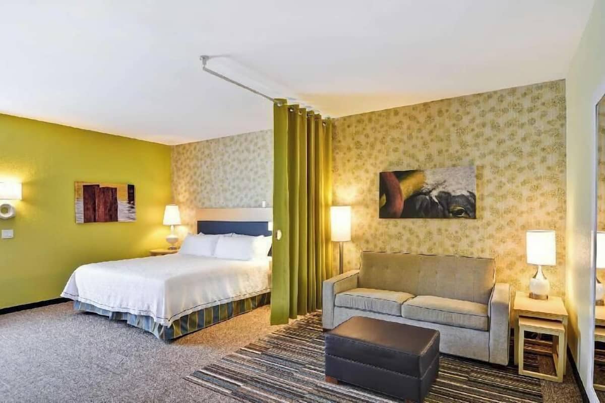 A hotel room with a bed, a sofa, a small table, a lamp, and a painting on the wall.