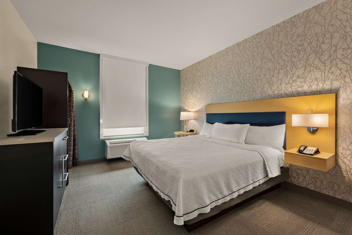 A hotel room with a bed, a TV, a desk, and a nightstand with a lamp and phone.