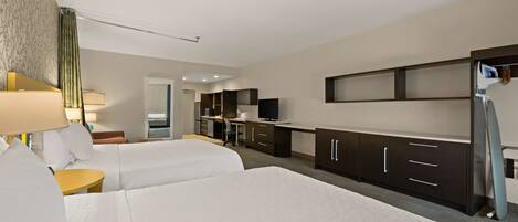 A hotel room with two beds, a desk, a chair, a TV, and a kitchenette.