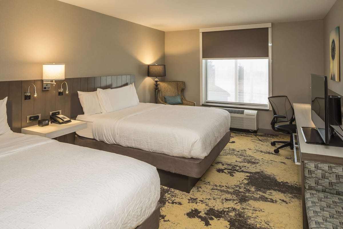 A hotel room with two beds, a desk, a chair, a TV, and a window with a view.