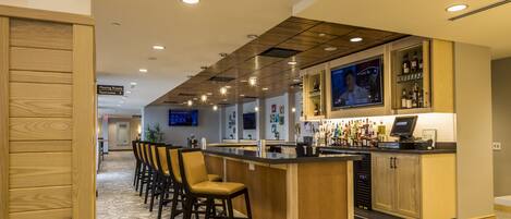 A modern bar area with a long counter, bar stools, and a television screen.