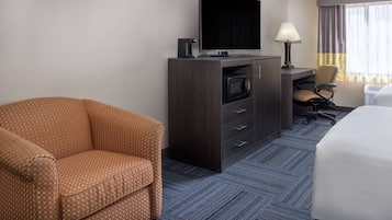 Una habitación de hotel con sofá, televisor en mueble bajo, escritorio y silla, y cama.