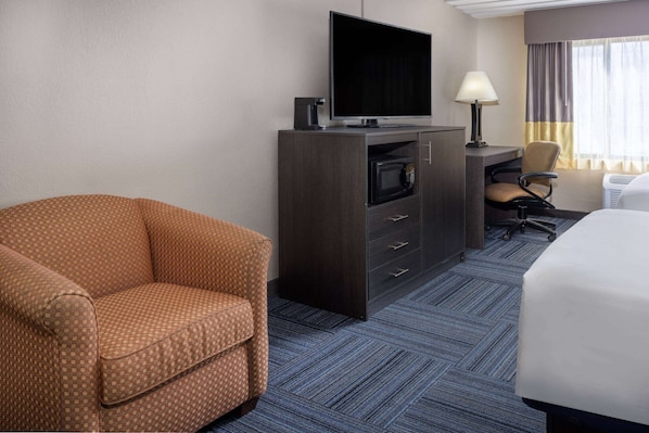 Una habitación de hotel con sofá, televisor en mueble bajo, escritorio y silla, y cama.