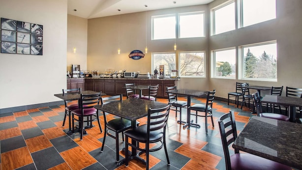 A spacious dining area with multiple tables and chairs, a kitchen in the background, and large windows providing natural light. - Baymont by Wyndham Appleton (Appleton)