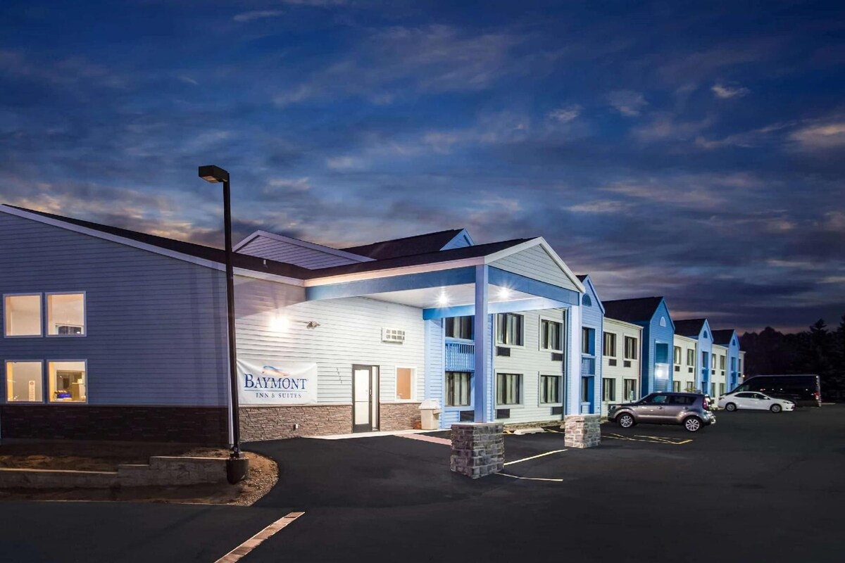 A Baymont Inn & Suites with a covered outdoor area, a parking lot, and a clear sky.