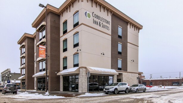 Edificio de Cobblestone Inn & Suites con fachada de ladrillo, ventanas grandes y suelo cubierto de nieve.