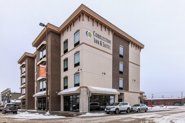 A Cobblestone Inn & Suites building with a brick facade, large windows, and a snow-covered ground.