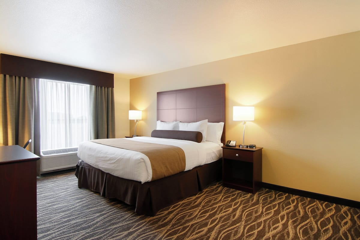 A hotel room with a large bed, two bedside lamps, a nightstand, a desk, and a window with curtains.