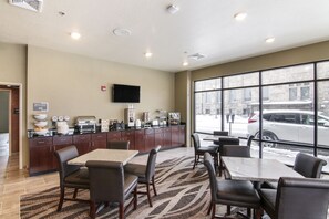 A hotel dining area with a kitchen counter, seating, and a large window with a view of the street.