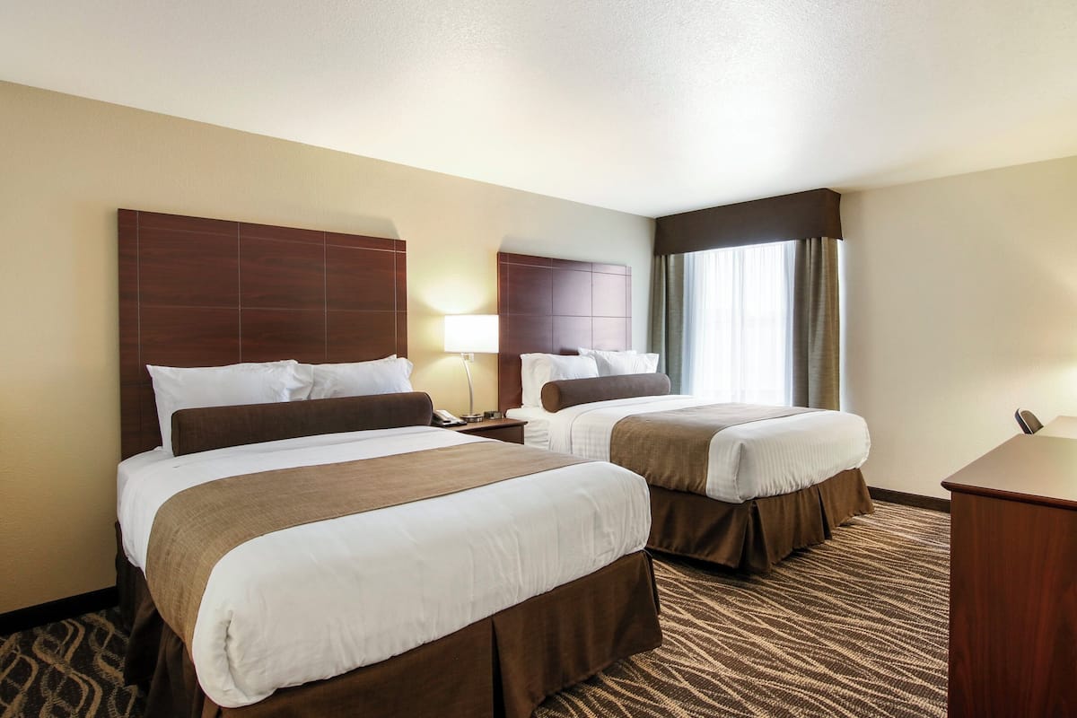 A hotel room with two beds, a desk, a lamp, and a window with curtains.