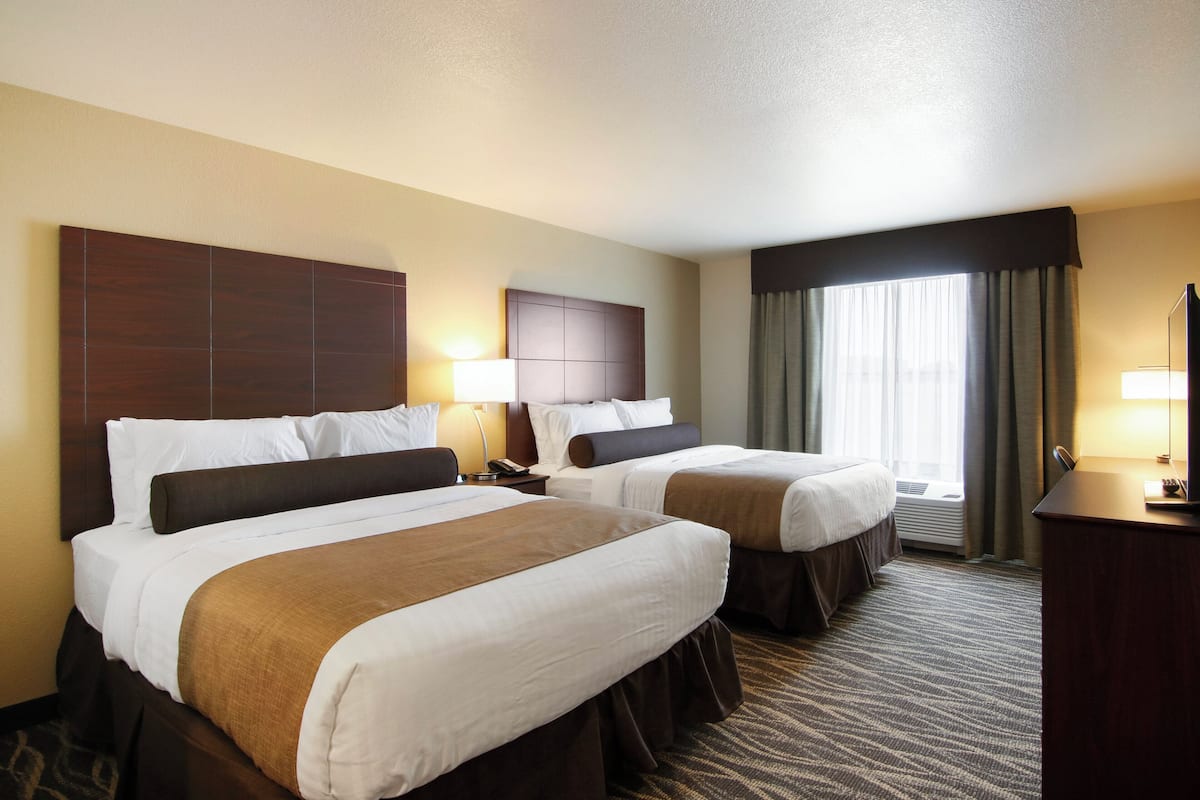 A hotel room with two beds, a desk, a lamp, and a window with curtains.