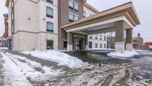 Entrada de hotel con un camino cubierto, nieve en el suelo y fachada de ladrillo.
