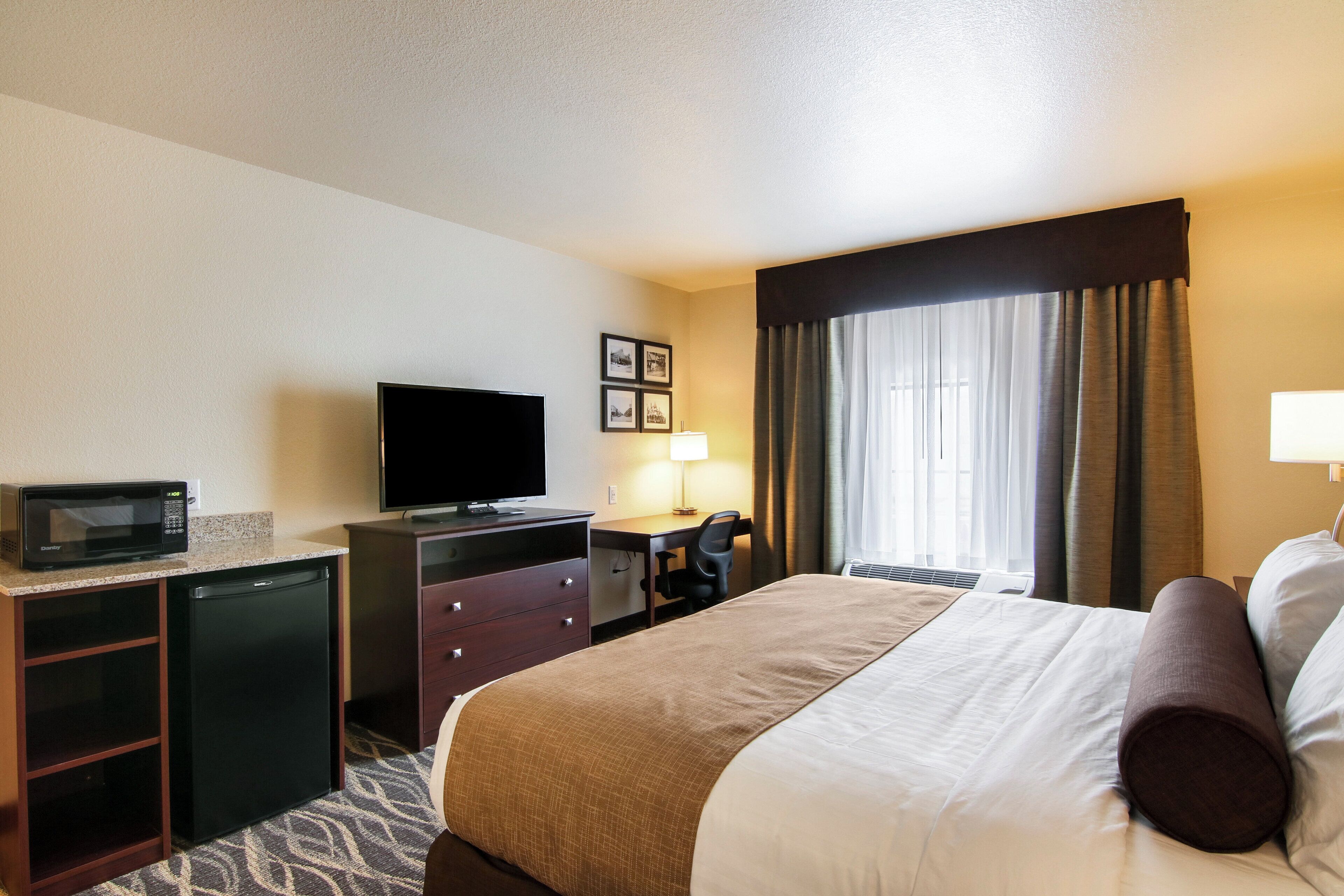 A hotel room with a bed, a desk with a computer, a television, a microwave, and a small refrigerator.