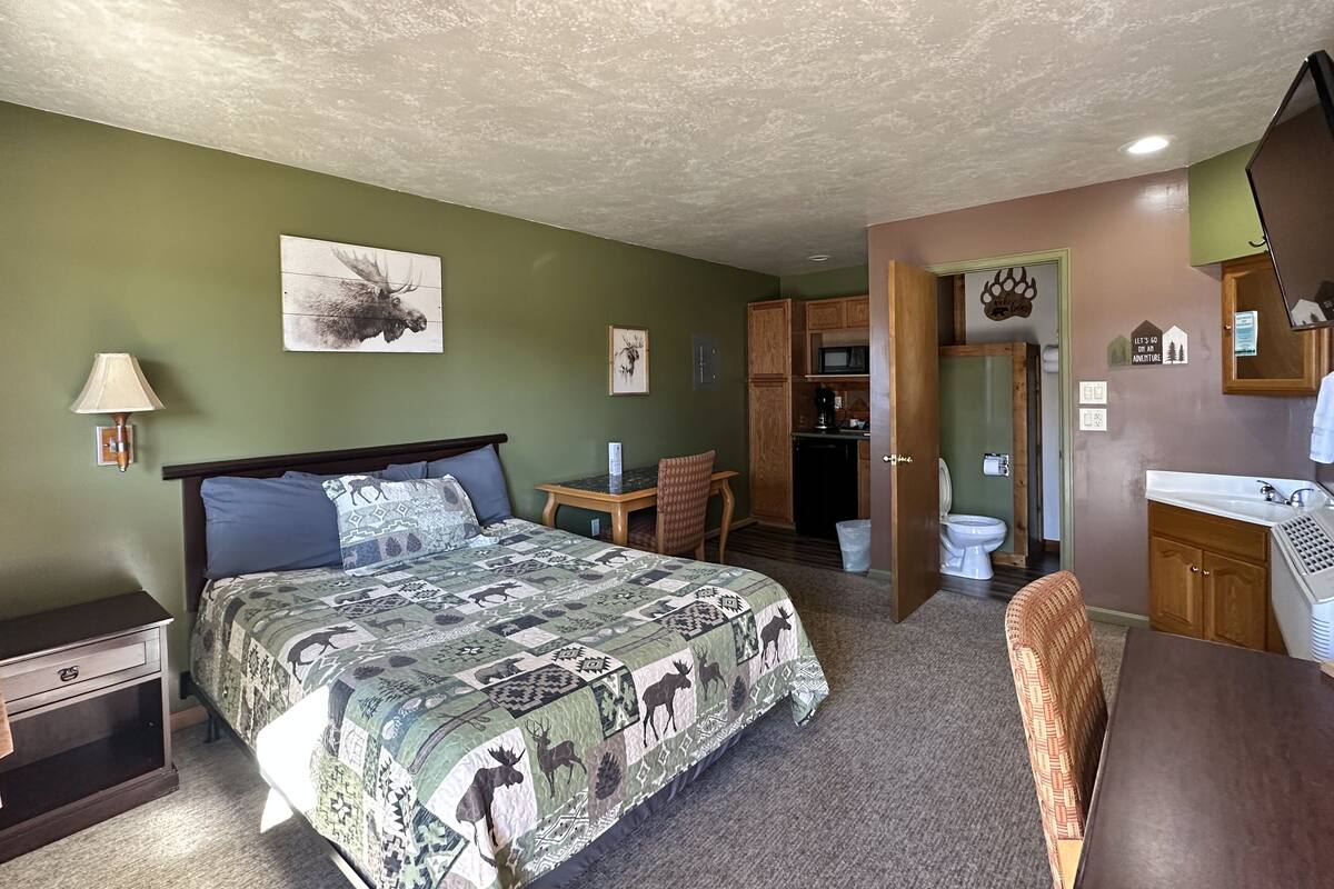 Un dormitorio con cama, escritorio, silla, kitchenette y baño.