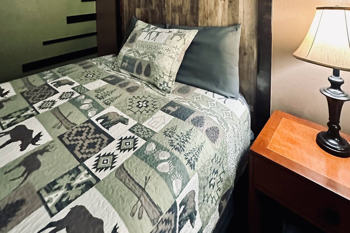 Un dormitorio con cama, mesita de noche, lámpara, un letrero en la pared y cabecera de madera.