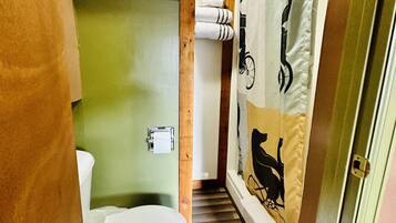A narrow bathroom with a toilet, a towel rack, and a shower curtain with a bear design.