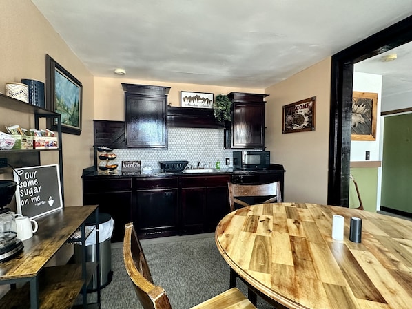 A compact kitchen with dark wooden cabinets, a round wooden table, and a chalkboard sign.