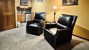 A room with two leather chairs, a kitchen area, a door, a lamp, and a framed picture on the wall. - Moosehead Lodge & Cabins (Rangely)