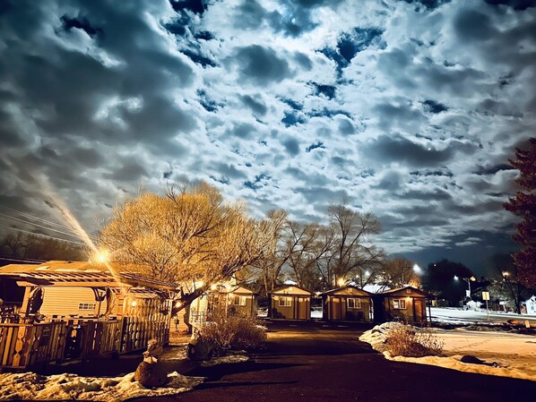 A row of cabins with a snowy ground, a clear sky, and a street in the background.