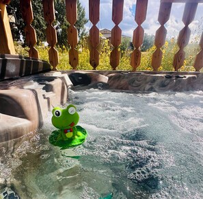 A hot tub with a frog toy in the water, surrounded by a wooden fence and yellow flowers.