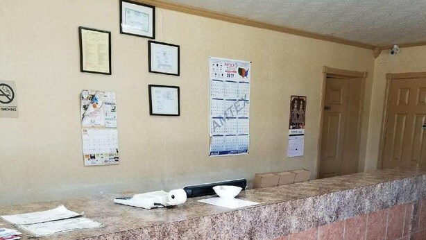 Un espace d’accueil avec un comptoir en marbre, un paillasson noir à l’entrée et plusieurs certificats encadrés accrochés au mur.