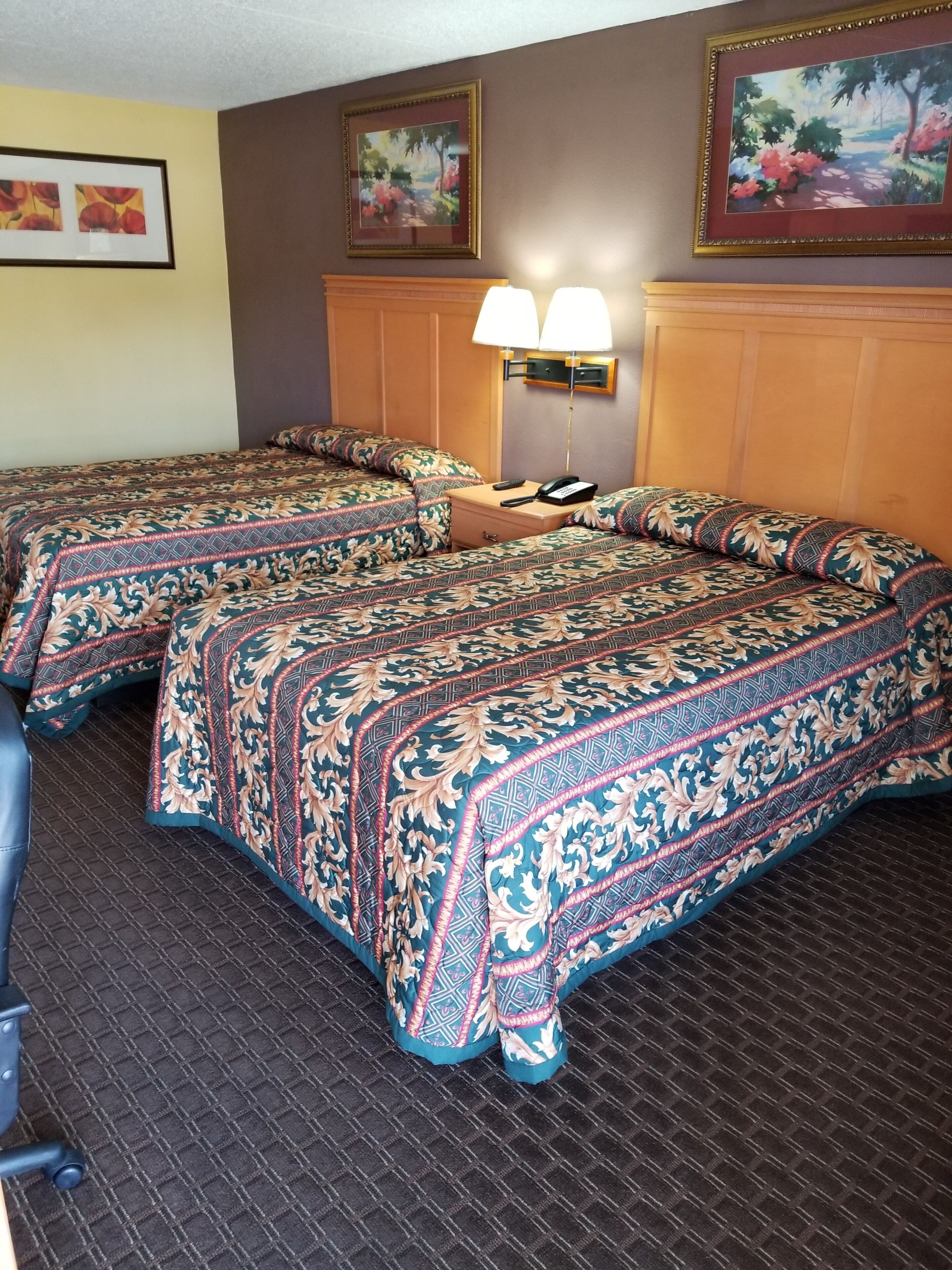 Quarto de hotel com duas camas, uma mesa de cabeceira com abajur e obras de arte nas paredes.