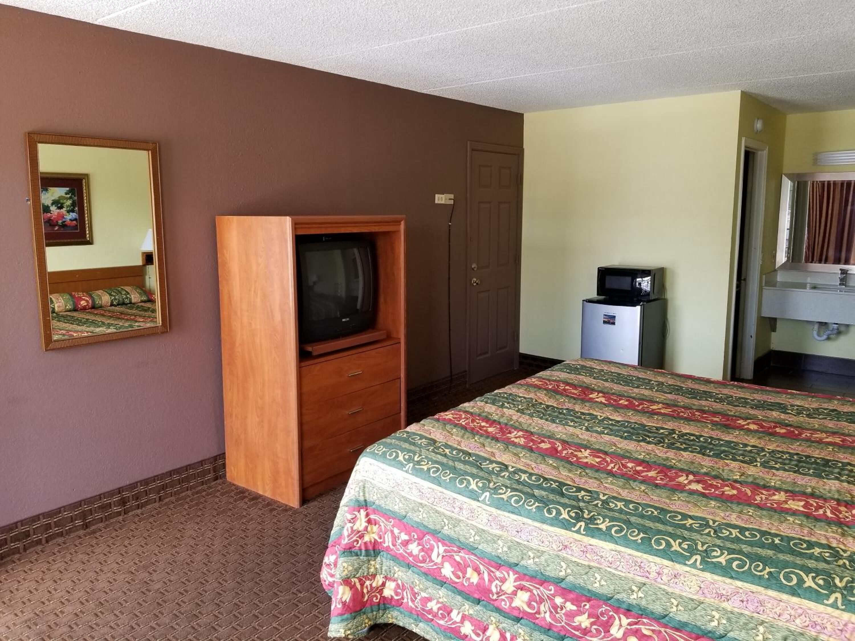 Een hotelkamer met een bed, een houten tv-meubel, een magnetron en een badkamer met een wastafel en spiegel.