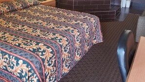 Une chambre d’hôtel avec un grand lit, un coin salon comprenant un fauteuil, une petite table, une lampe fixée au mur, un téléphone et une salle de bain avec une baignoire et un miroir.