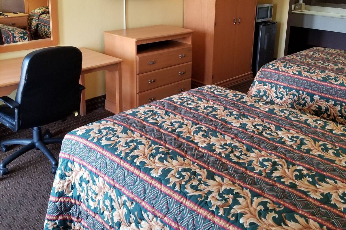 A hotel room with a bed, a desk, a chair, a wardrobe, a television, and a mirror.