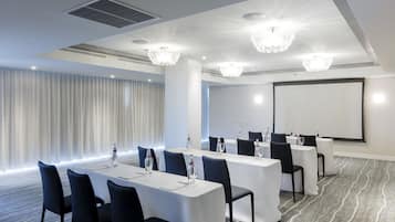 Un salón de conferencias con mesas blancas, sillas negras y candelabros.