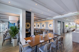Un restaurante moderno con una larga mesa de madera, varias áreas de estar y una gran planta en maceta.